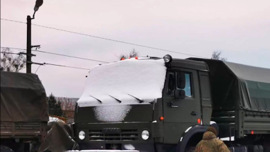 Заснеженные военные грузовики на платформах, военнослужащий у состава
