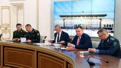 Совещание за столом: военные и гражданские участники, на экране здание
