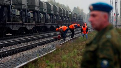 Рабочие в оранжевых жилетах у путей рядом с воинским эшелоном, на переднем плане военнослужащий в голубом берете