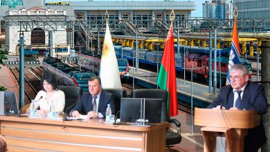 Президиум собрания за столом и выступающий за трибуной на фоне флагов
