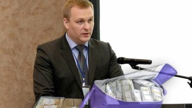 Мужчина у трибуны с микрофоном, на переднем плане сумка с пачками денег