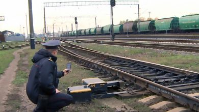 Работник в форме у измерительного прибора на пути, вдали грузовой состав