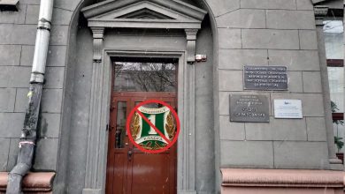 Вход в административное здание с табличками, на двери перечёркнутая эмблема
