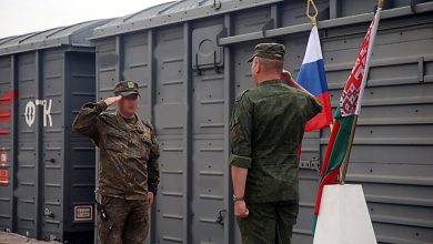 Двое военнослужащих отдают честь у флагов России и Беларуси на фоне крытых вагонов