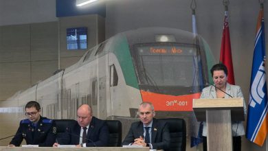 Совещание: президиум за столом и выступающая за трибуной на фоне изображения электропоезда